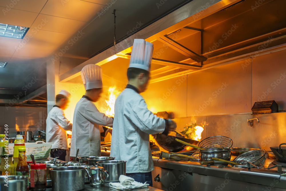 餐厅厨房里的厨师拿着平底锅在炉子旁，在食物上做火烈鸟