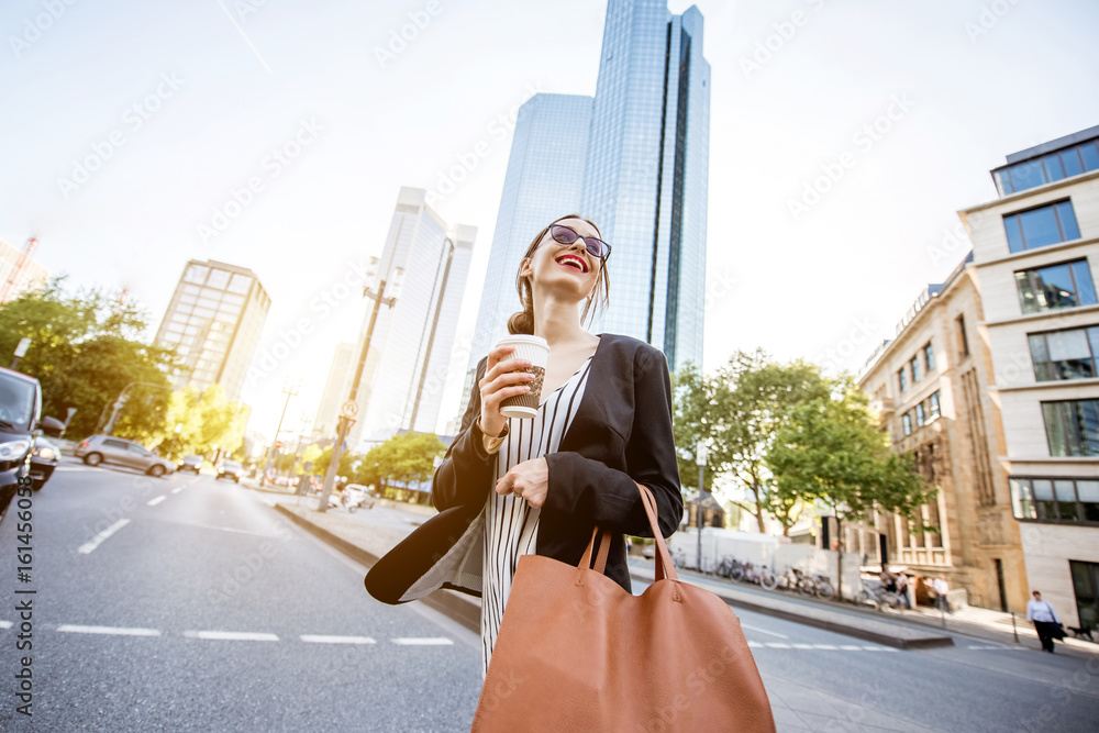 年轻的女商人拿着袋子和咖啡穿过法兰克福现代区的街道