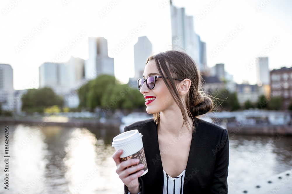 Young businesswoman having a coffee break outdoors sitting on the bridge in Frankfurt city