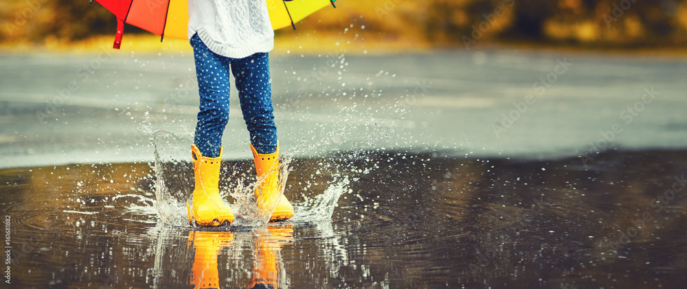穿着黄色橡胶靴的孩子在雨中跳过水坑