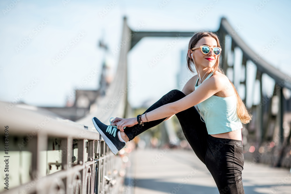 一名身穿运动服的年轻女子在法兰克福市的铁桥上晨练伸展运动