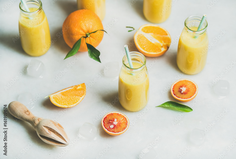 健康的黄色奶昔，配柑橘类水果、生姜、装在玻璃瓶里的冰，放在浅色大理石桌子后面