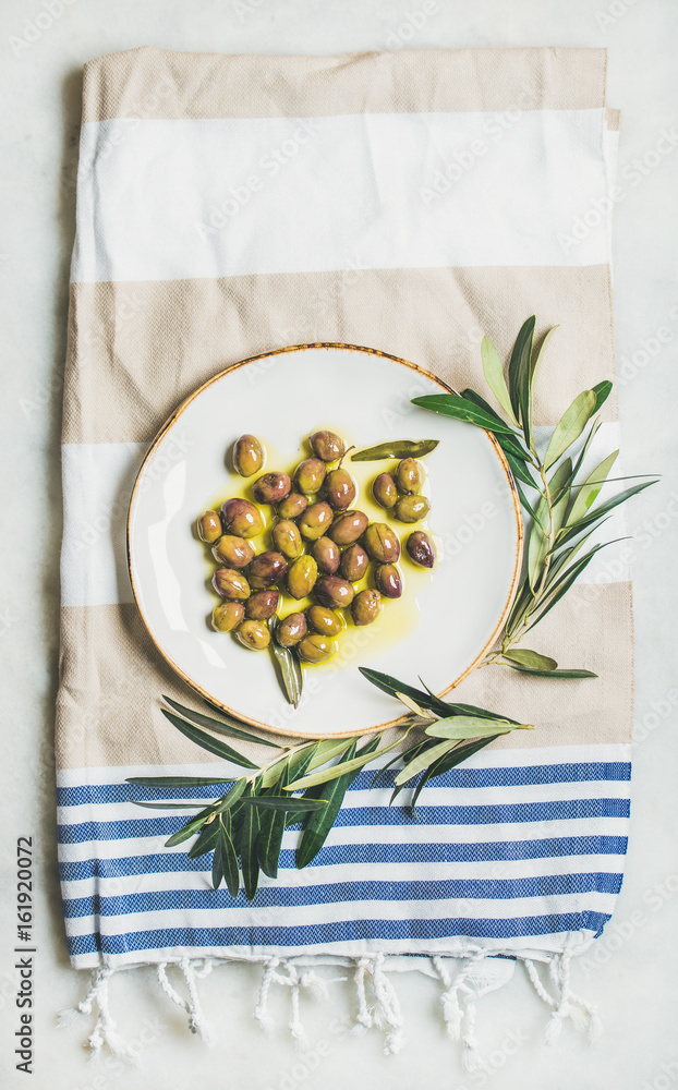 在白色陶瓷盘子和橄榄树上用天然初榨橄榄油腌制的绿色地中海橄榄