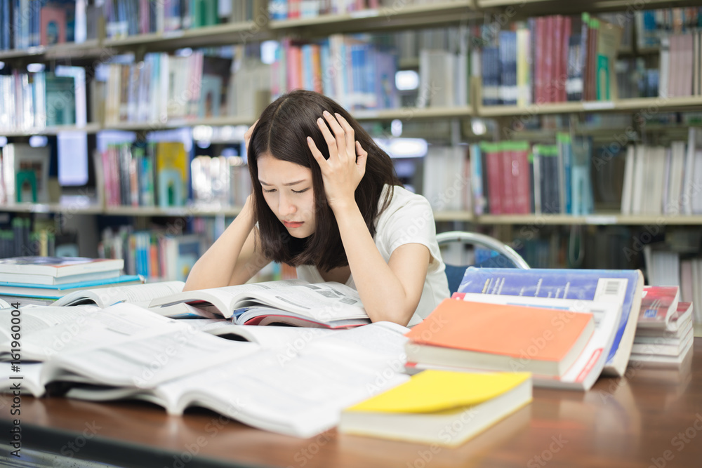 年轻的亚洲学生在大学图书馆读书备考时承受着精神压力