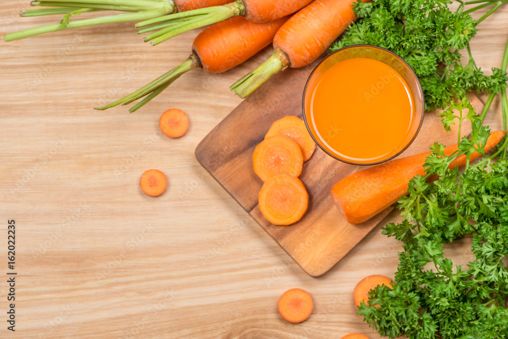 一杯新鲜的胡萝卜汁和蔬菜放在木桌上。