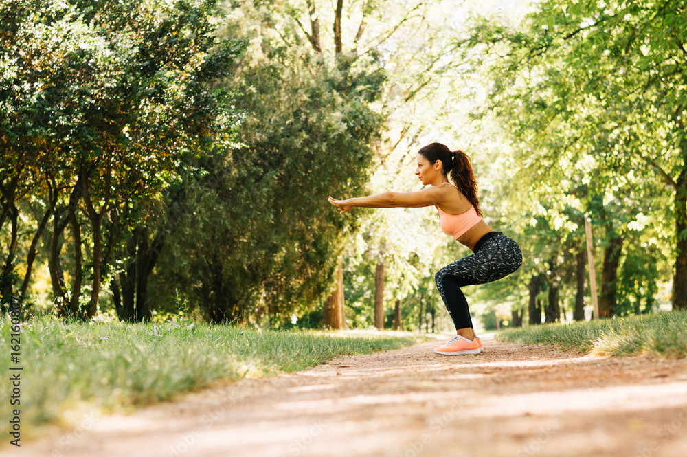 Young female athlete doing squat exercises outdoors in park.