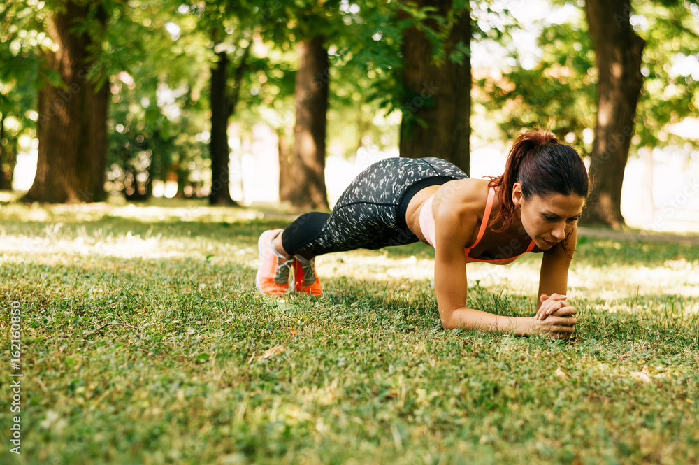 Fit young woman doing the plank exercise in park