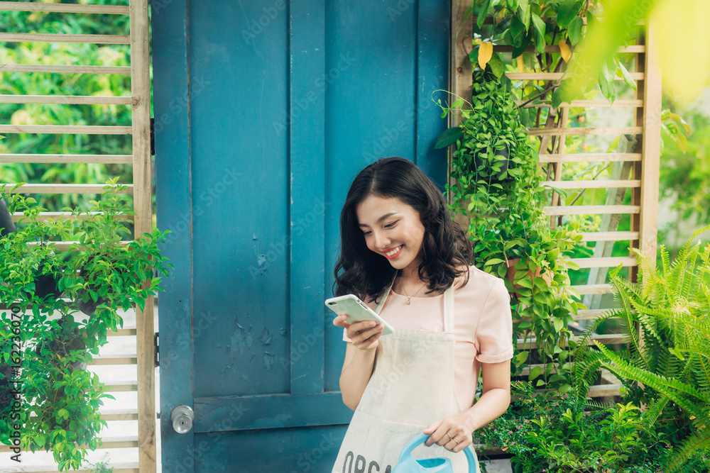 年轻的亚洲女性使用智能手机，一边给植物浇水一边打电话