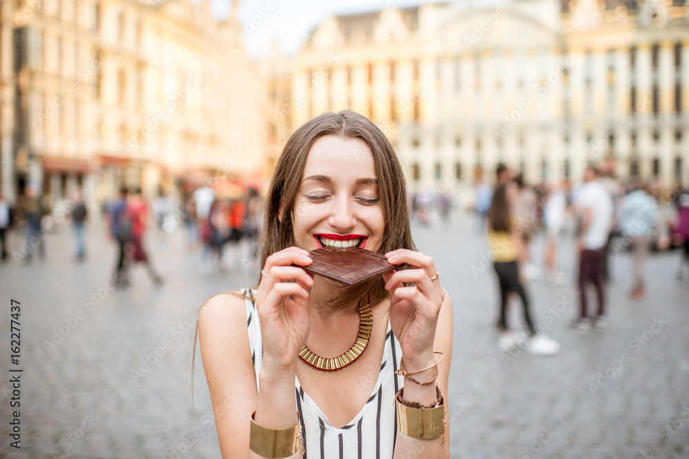 年轻快乐的女人拿着黑巧克力棒站在布鲁塞尔的大广场上
