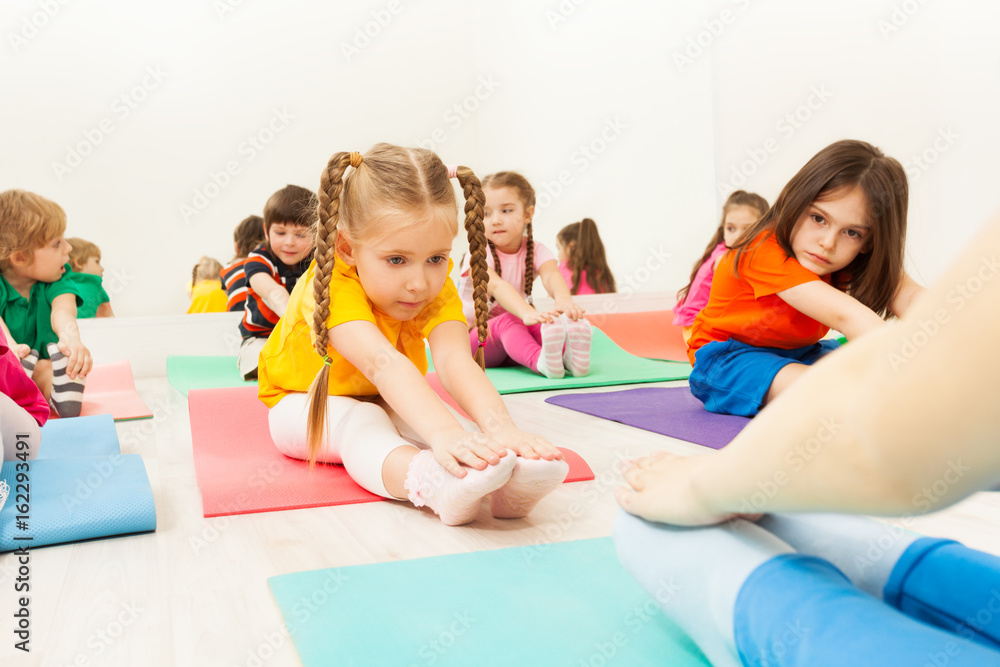 Diligent girl doing stretching exercise on mat