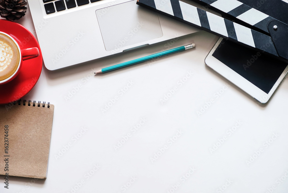 白色桌面上有电影拍板笔记本电脑和咖啡杯笔记事本的办公室用品。