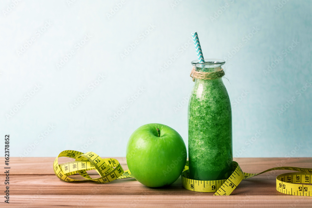 木桌上的玻璃瓶里装着健康的新鲜绿色奶昔汁，里面有绿色苹果和绿色