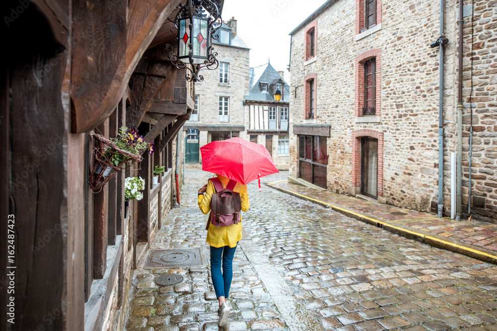 法国布列塔尼地区迪南村，一名身穿黄色雨衣的年轻女子撑着伞行走