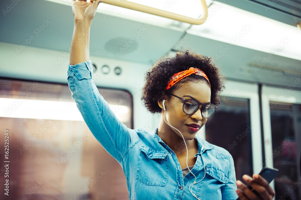 微笑的非洲年轻女子在地铁上听音乐