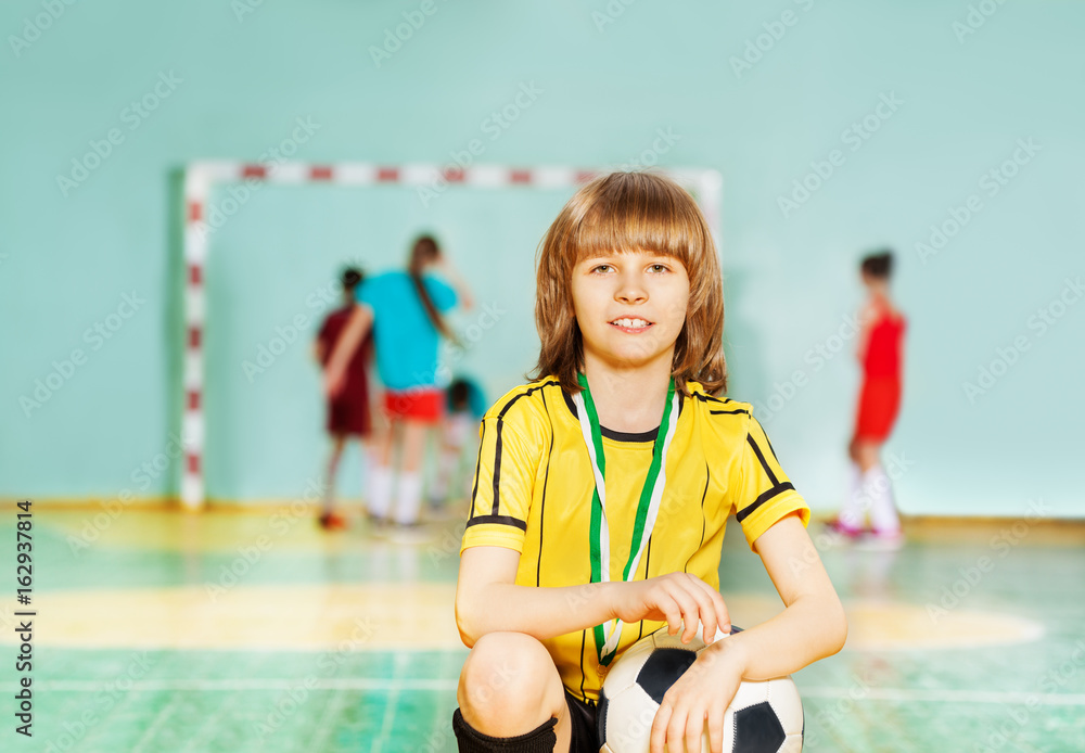Happy boy sitting with soccer ball in sports hall