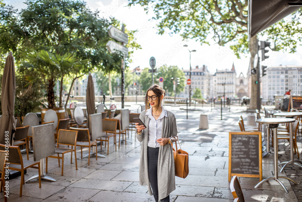 年轻时尚的女商人拿着手机和包走在里昂老城区咖啡馆的街上