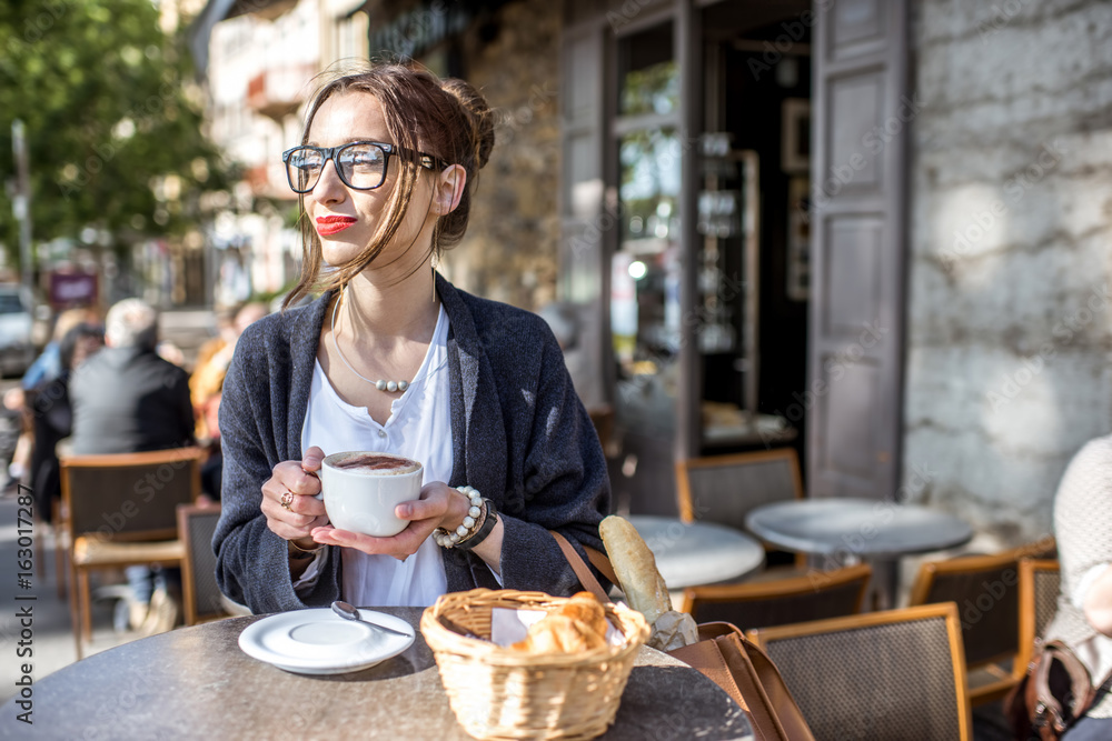 一位年轻女士坐在里昂的法国咖啡馆户外吃早餐，配咖啡和羊角面包
