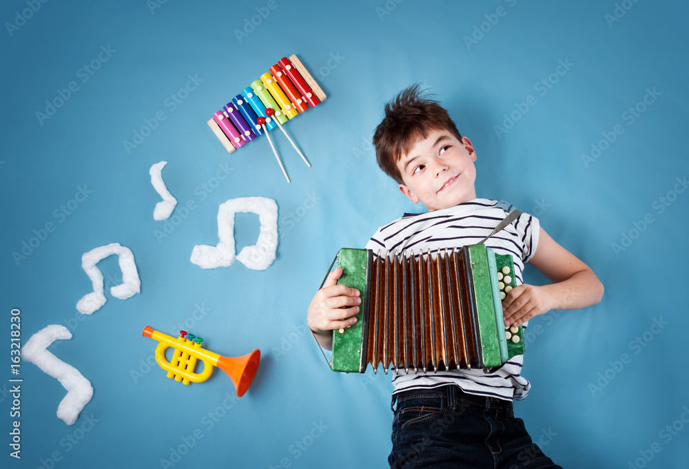 快乐的七岁男孩，蓝色毯子背景，手风琴和音符。年幼的孩子