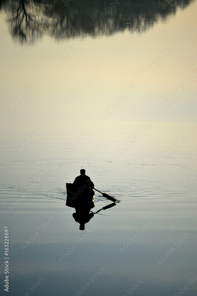 河流的镜面，一个渔夫坐在船上，早上去钓鱼