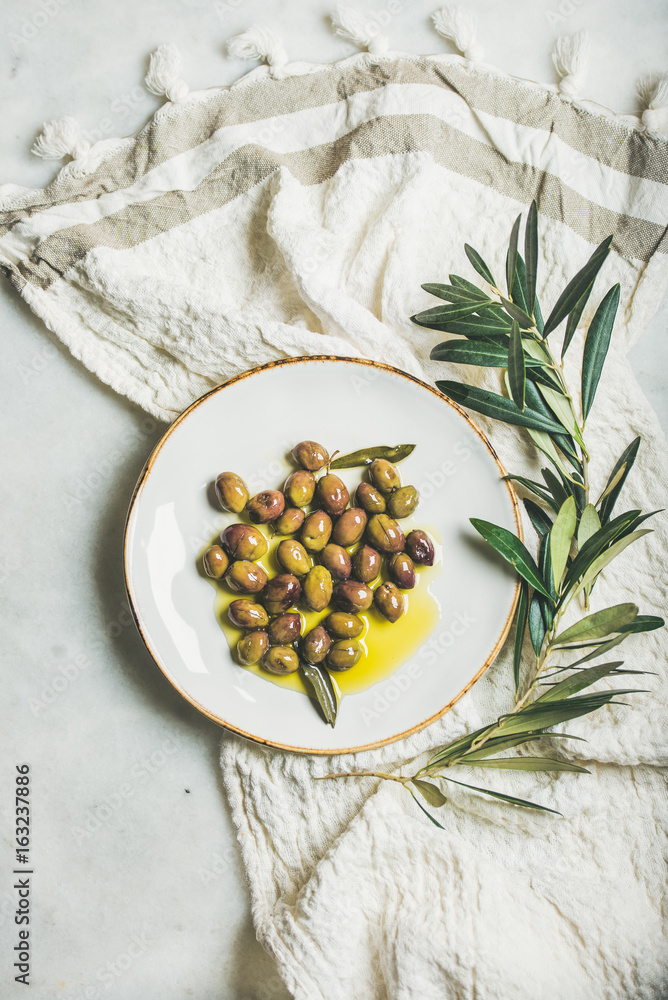 Pickled green Mediterranean olives in virgin olive oil on white ceramic plate and olive tree branch 
