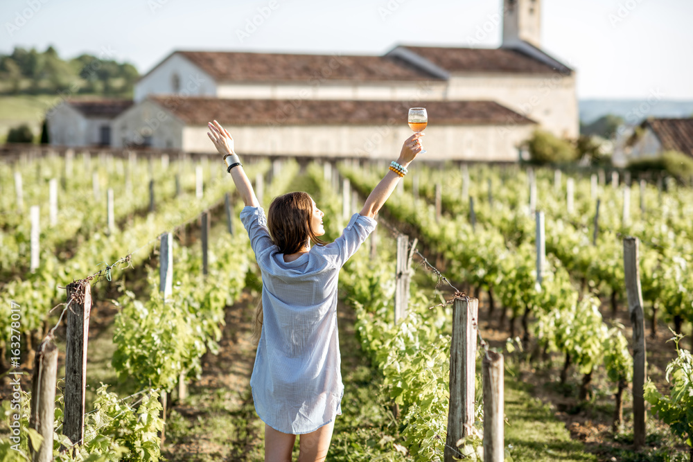 Young woman with glass of wine enjoying beautiful sunset view on the vineyard in Bordeaux region in 