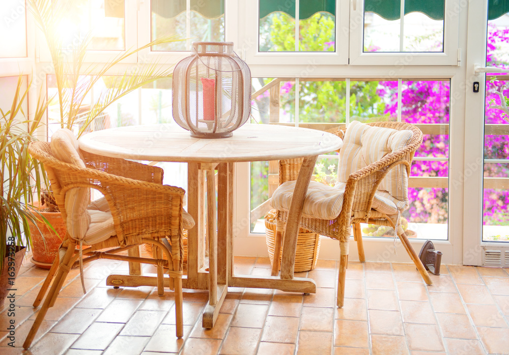阳光明媚、空荡荡的夏季咖啡馆露台内部，配有桌子和柳条椅