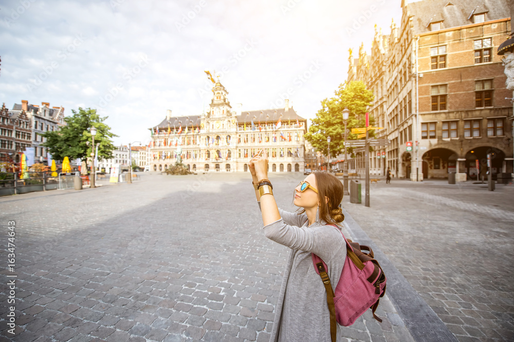 Young woman tourist photographing wiht phone on the Great Market square in Antwerpen, Belgium