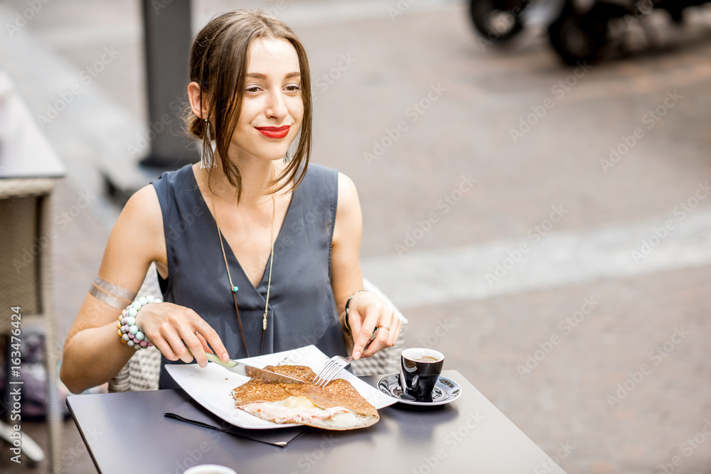 Young woman having a breakfast with french pancakes called galette sitting at the restaurant outdoor