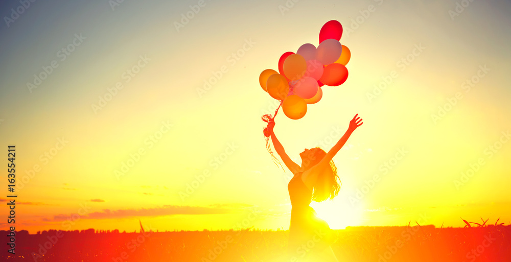 美丽的女孩在晴朗的天空中带着五颜六色的气球在夏日的田野上奔跑和跳跃