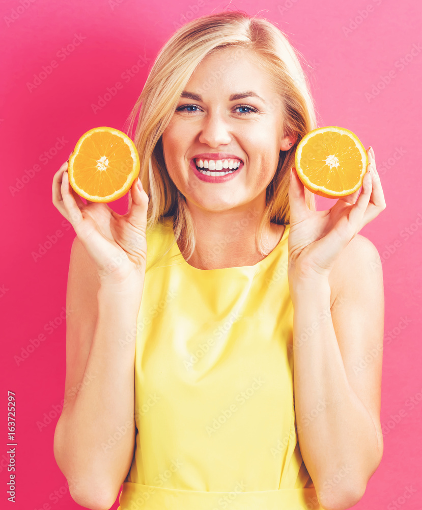 粉红色背景下拿着两半橙子的快乐年轻女人