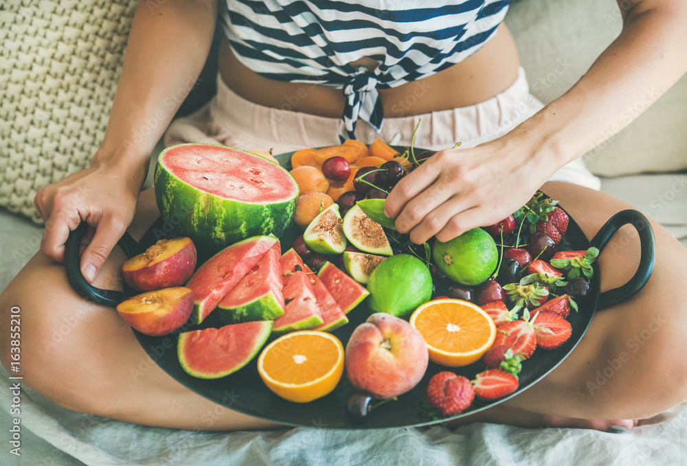 夏季健康生素食主义者在床上吃早餐的概念。穿着条纹家居衬衫的年轻女孩