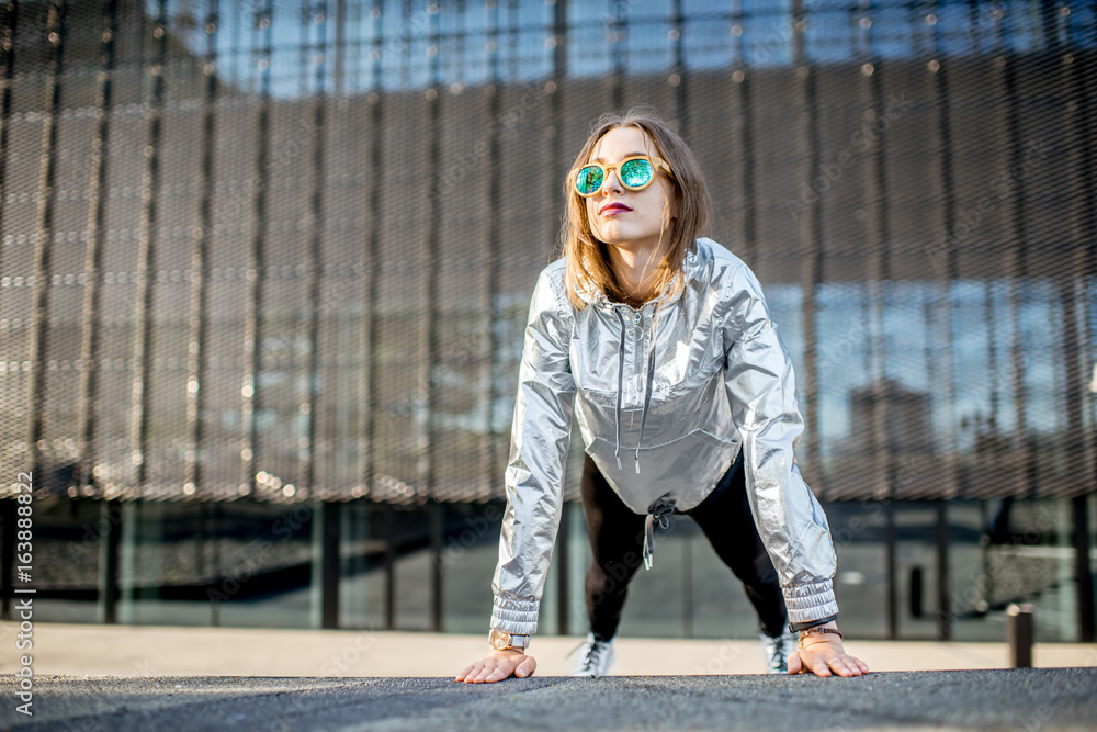 一位穿着银色夹克的时尚女性在现代城市环境中户外锻炼的生活方式画像