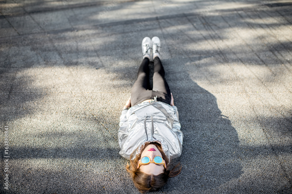一位穿着银色夹克和鞋子的现代女性躺在户外柏油路上的生活方式画像