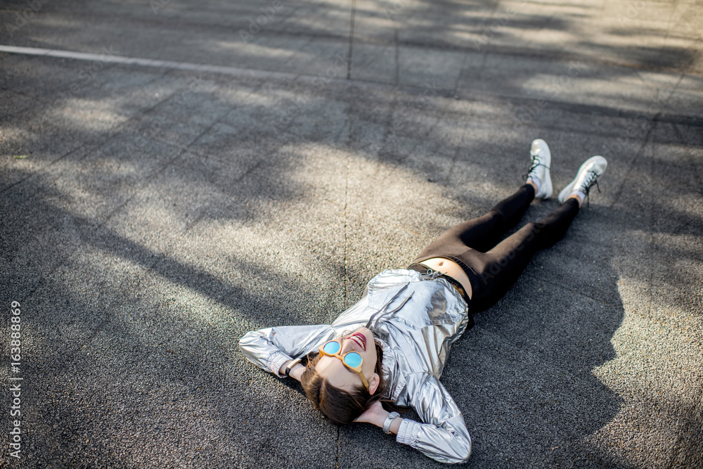 一位穿着银色夹克和鞋子的现代女性躺在户外柏油路上的生活方式画像