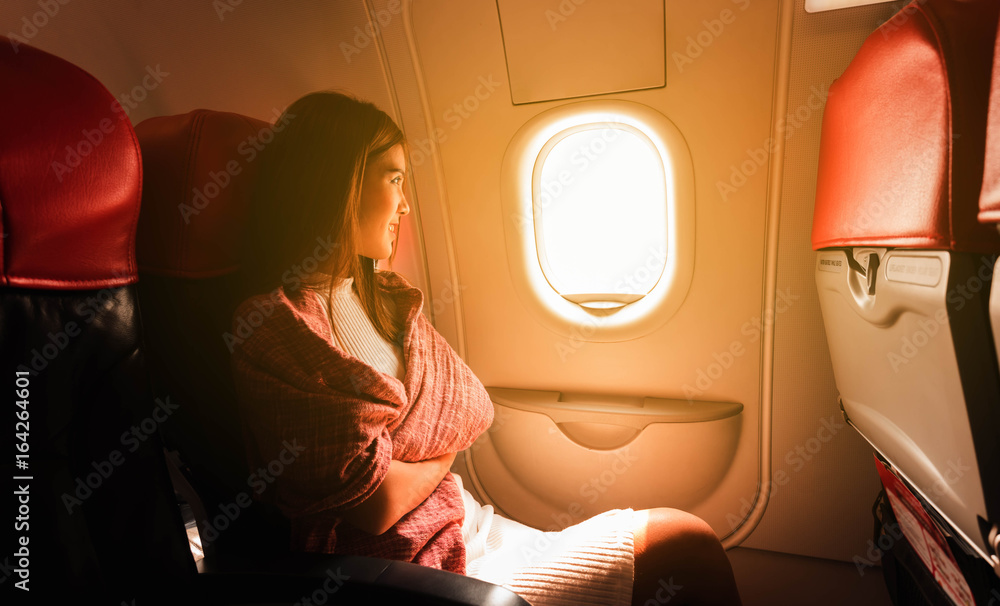 年轻漂亮的女人在飞行中坐在飞机的窗户边