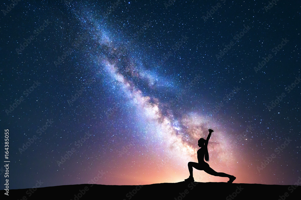 银河系，有一个站着的女人在球场上练习瑜伽的剪影。美丽的风景