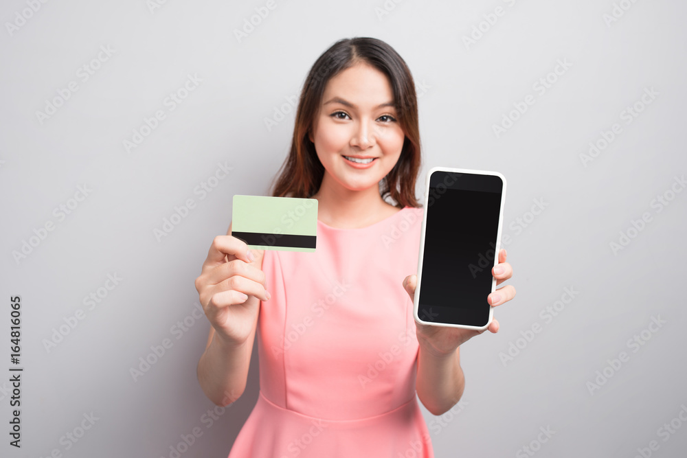 魅力亚洲女性手持智能手机并出示信用卡。展示您的产品。