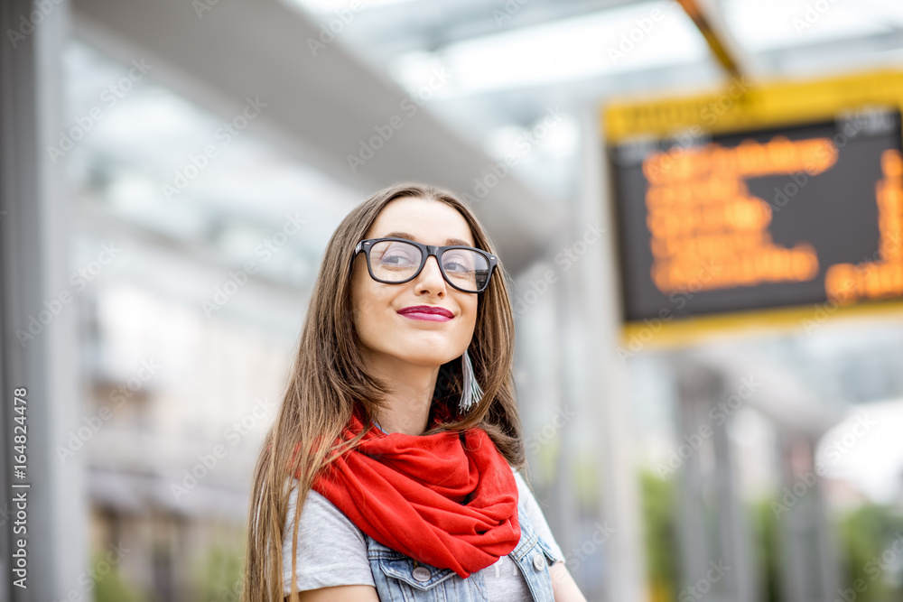 一位年轻女子站在有轨电车站上等待公共交通的画像，上面有时间表