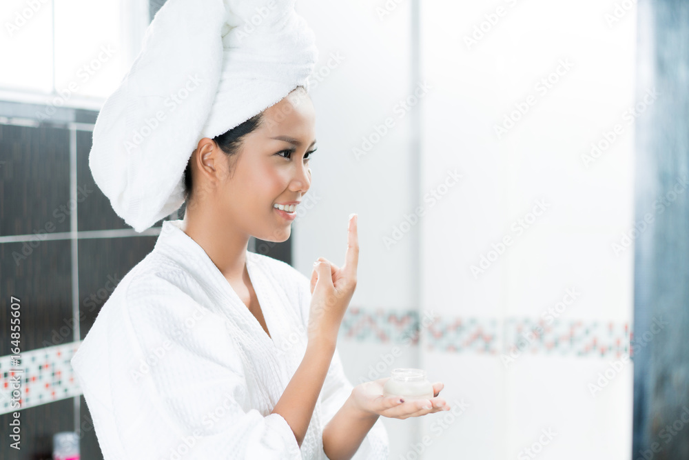 亚洲女性在浴室洗澡后，正在脸上涂面霜和乳液。