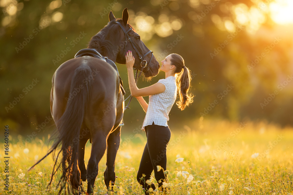 傍晚落日余晖中年轻女子牵着她的马