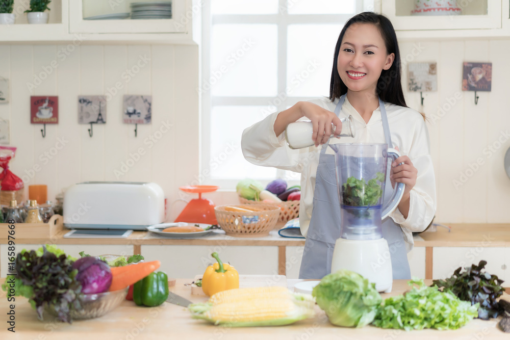 亚洲女性在家厨房用搅拌机制作绿色奶昔。健康的生食生活方式概念