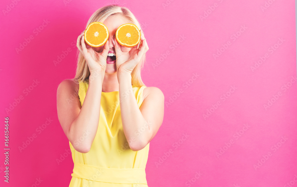 快乐的年轻女人在粉色背景上拿着两半橙子