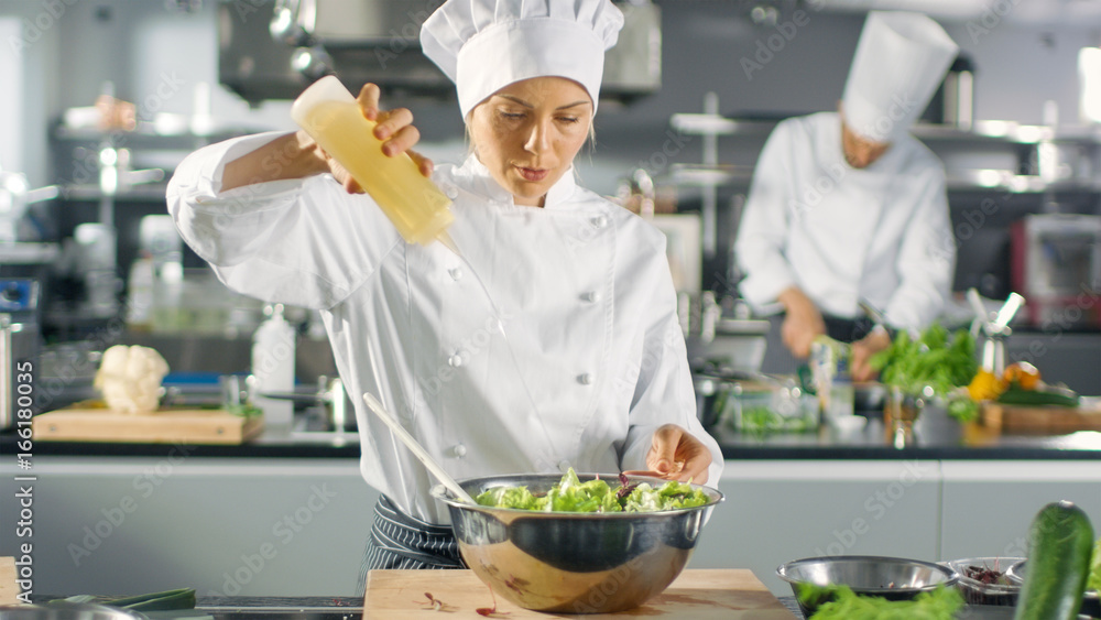 在一家著名的餐厅里，女厨师准备沙拉，广告油。她在一家现代化的大厨房工作。