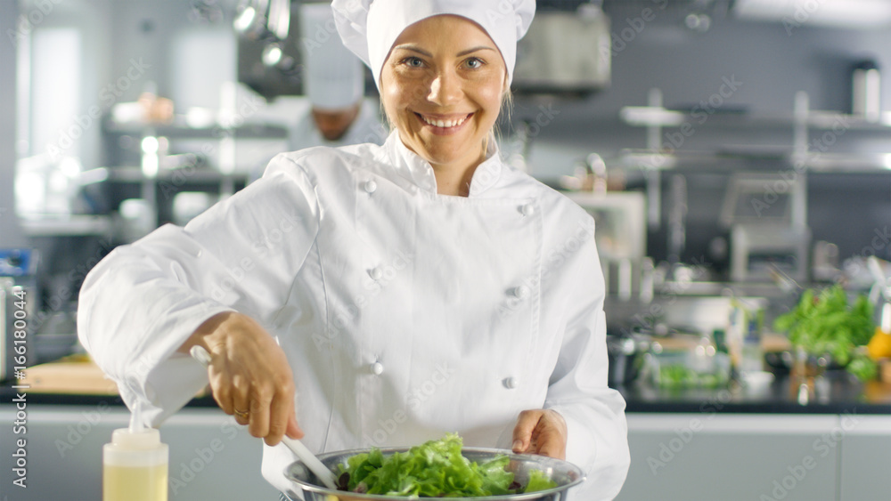 在一家著名的餐厅里，女厨师准备沙拉，对着镜头微笑。她在一家大型现代餐厅工作