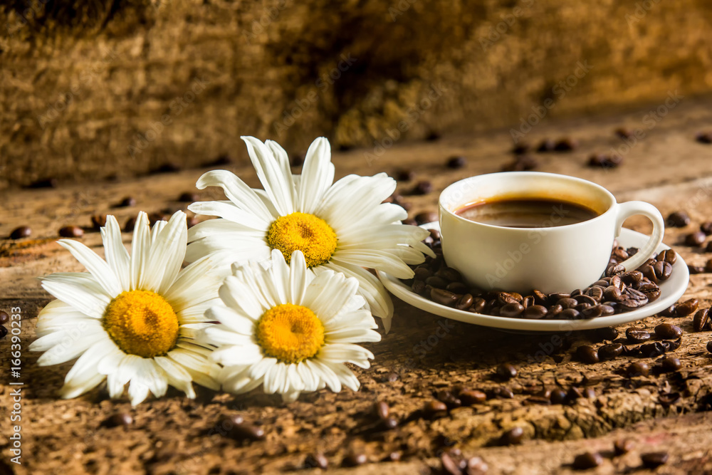 Coffee cup and fried Coffee beans on a wooden table with beautiful white flowers on a wood backgroun