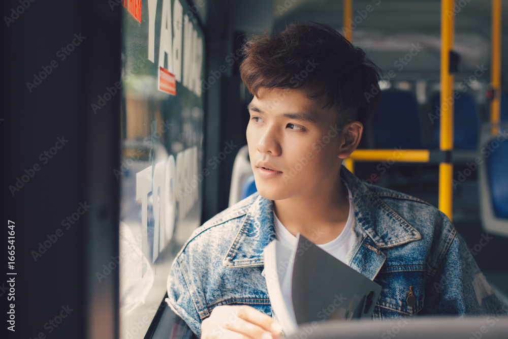 一个年轻人坐在城市公交车上看书。