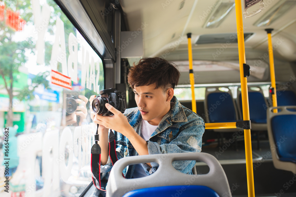 亚洲男游客从公交车车窗用数码相机拍摄城市视频