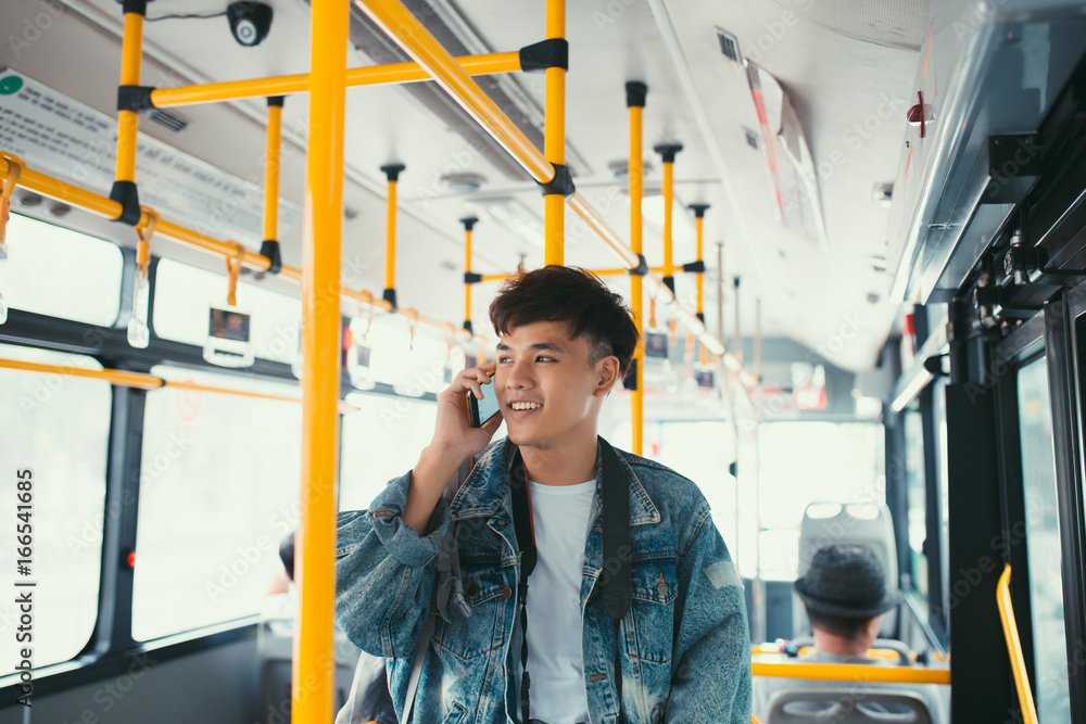 英俊的亚洲男子站在城市公交车上打手机