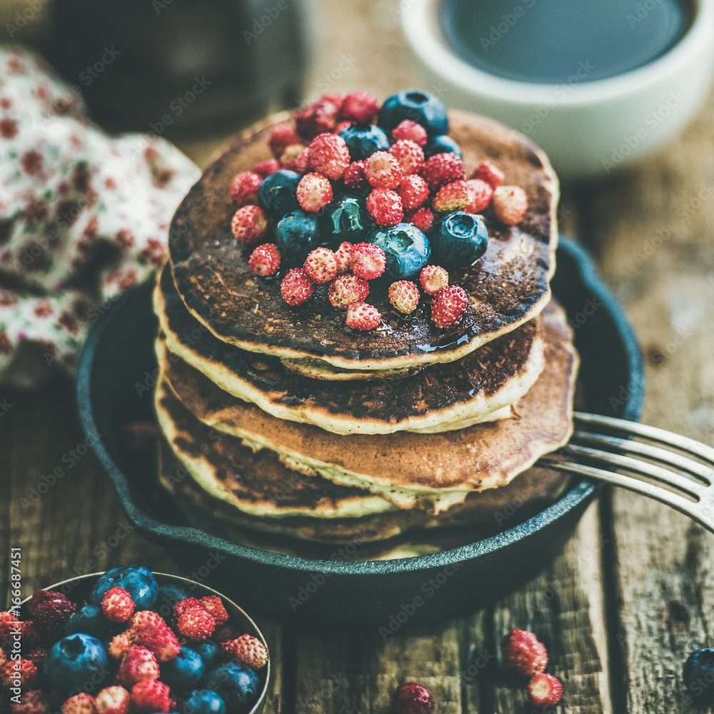Sweet breakfast with pancakes with fresh forest berries and honey in cast iron pan over rustic woode