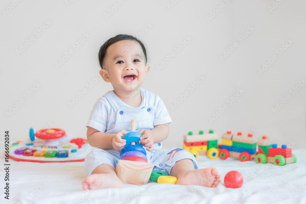 可爱的亚洲男婴9个月大，坐在床上，在家里玩彩色发育玩具。